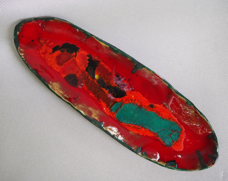 Opera in ceramica contemporanea con smalto rosso e inserti di vetro verde, superficie irregolare e segni di frattura materica.