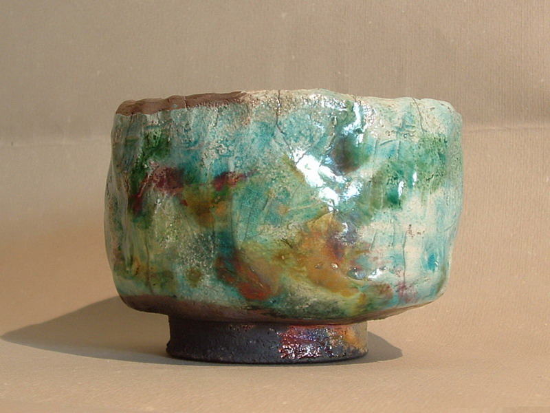 Tazza da tè in ceramica raku, con finitura irregolare e sfumature di verde e marrone.