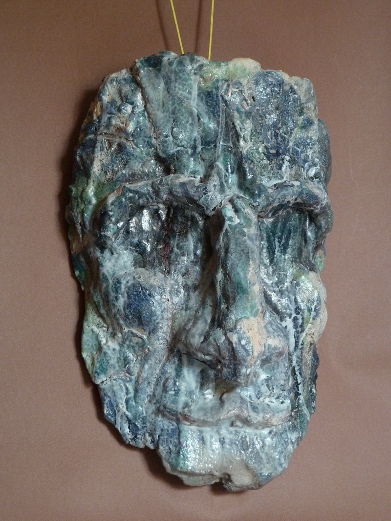 Dettaglio della maschera raku che mostra crepe, stratificazioni e cromie minerali, simbolo di un volto che affiora dalla materia grezza.