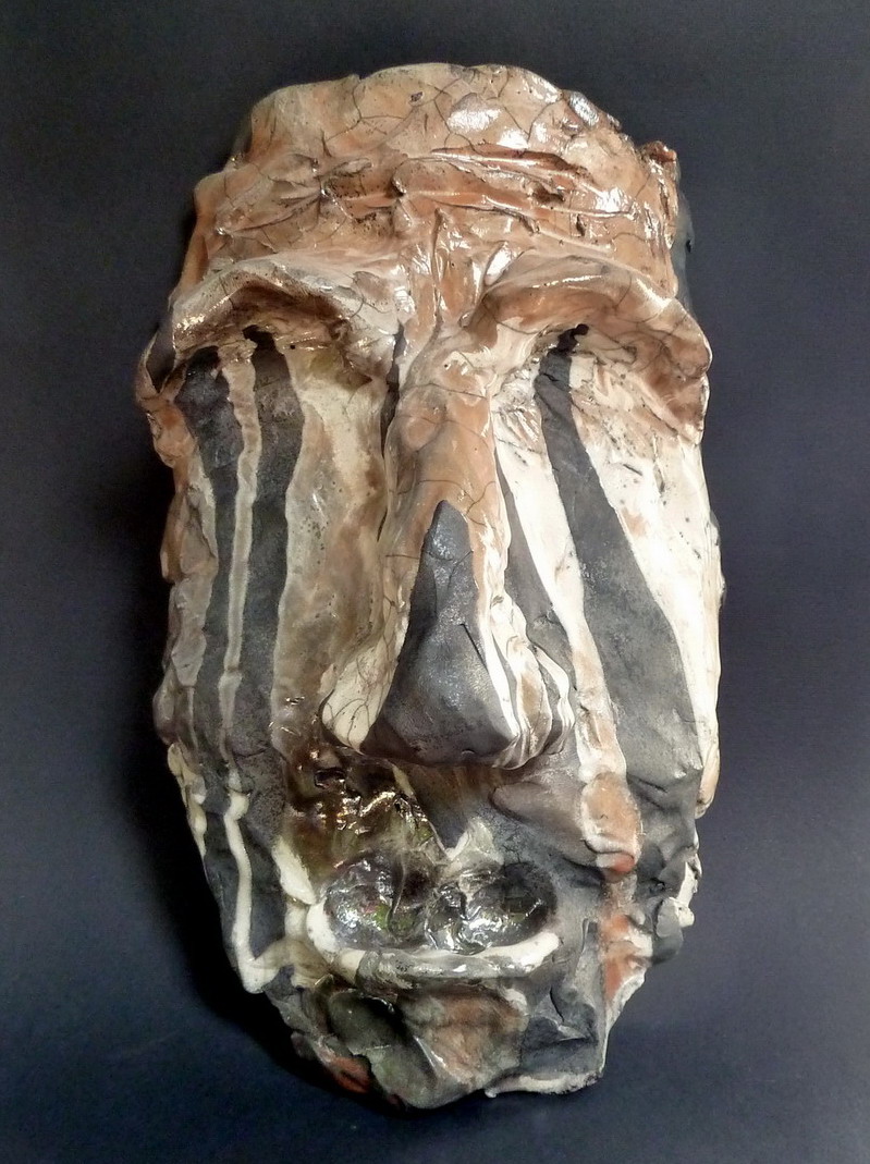 Scultura raku raffigurante un volto simbolico, modellato in argilla e trasformato dal fuoco in una superficie vibrante di crepe, ombre e trasparenze.